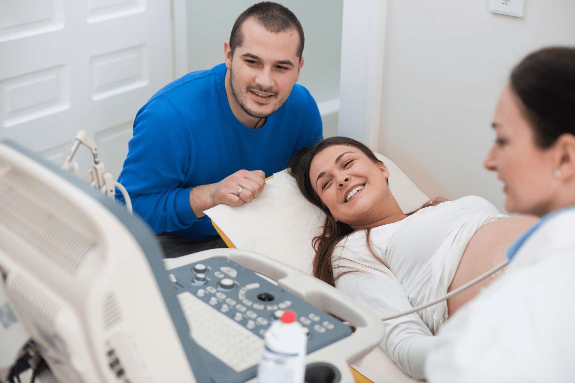 A couple watches their pregnancy ultrasound as the sonographer looks on